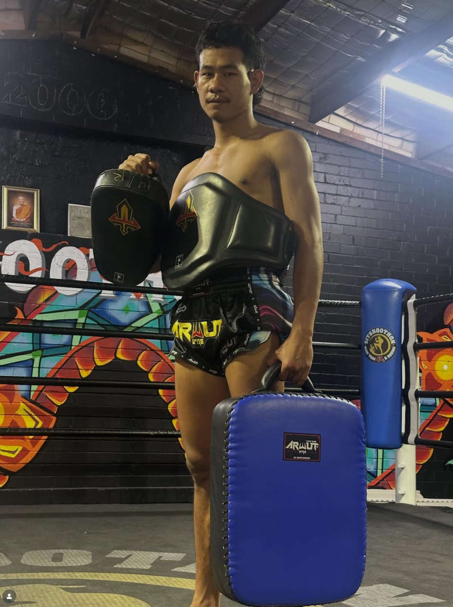 Male holding a thai pad and kick shield in a gym setting