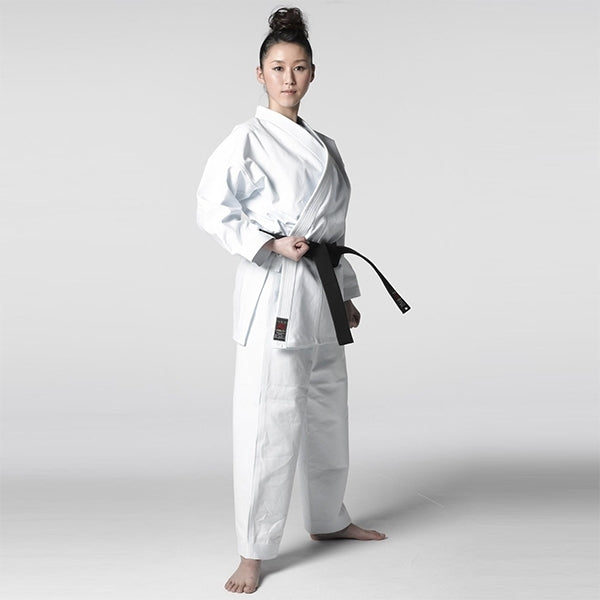 Woman wearing a white martial arts uniform with a black belt on a plain background
