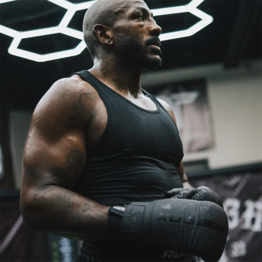 Muscular man in a black tank top and boxing gloves in a gym setting