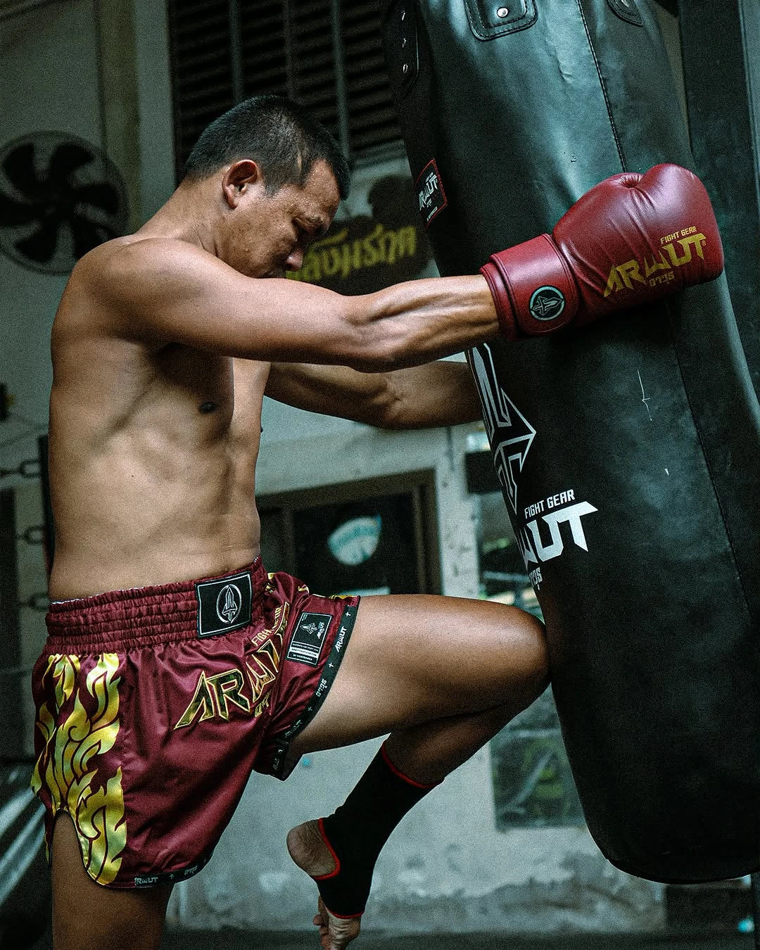Seksan wearing red boxing shorts and gloves, training with a punching bag.