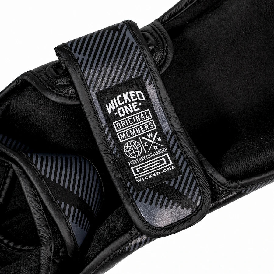 Close-up of a black martial arts grappling glove with a black and gray striped strap and a white 'Wicked One' brand label.