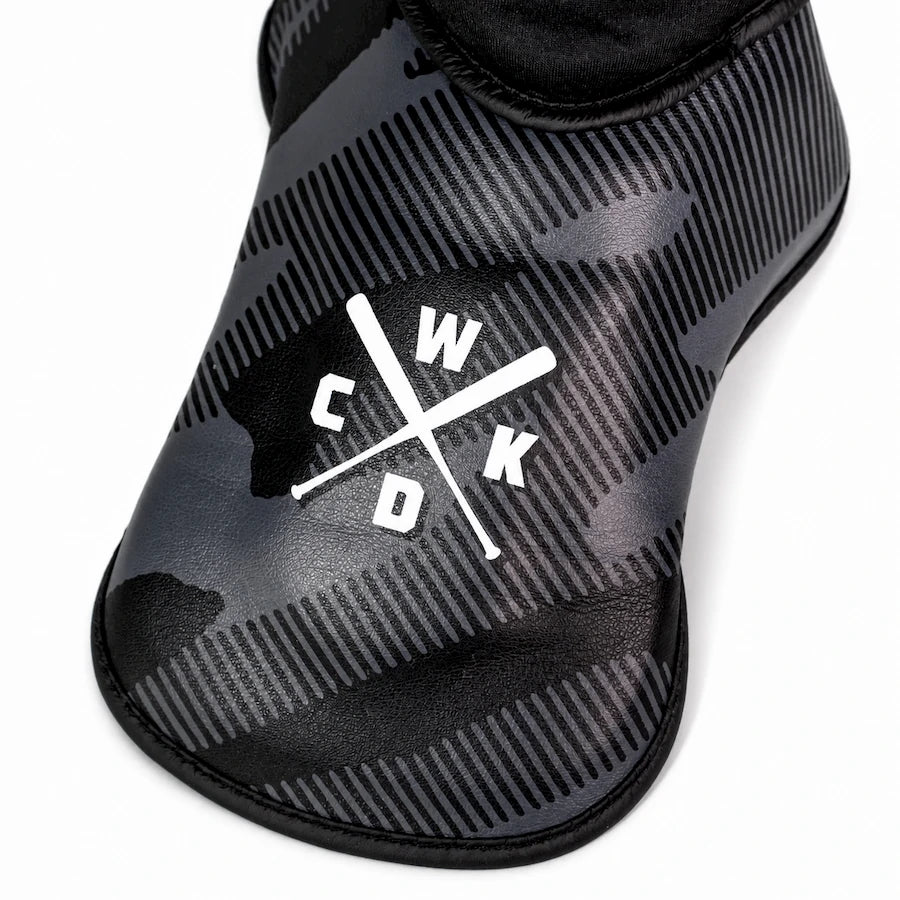 A close-up of a black and dark gray camo-patterned boot cover with a white crossed bats and 'WCKD' logo on the side, set against a plain white background.