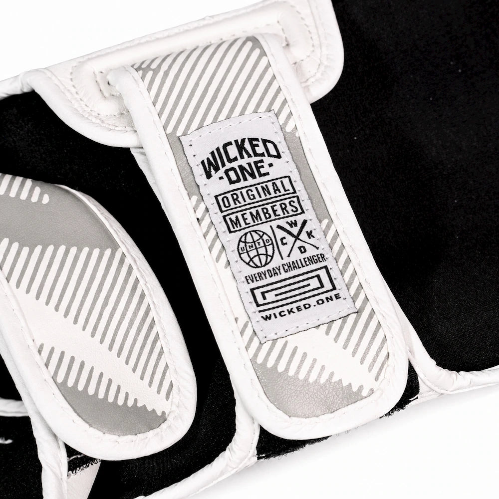 Close-up of a black and white protective shin guard showing the inner label that reads 'Wicked One Original Members' with a logo and 'Everyday Challenger' text.