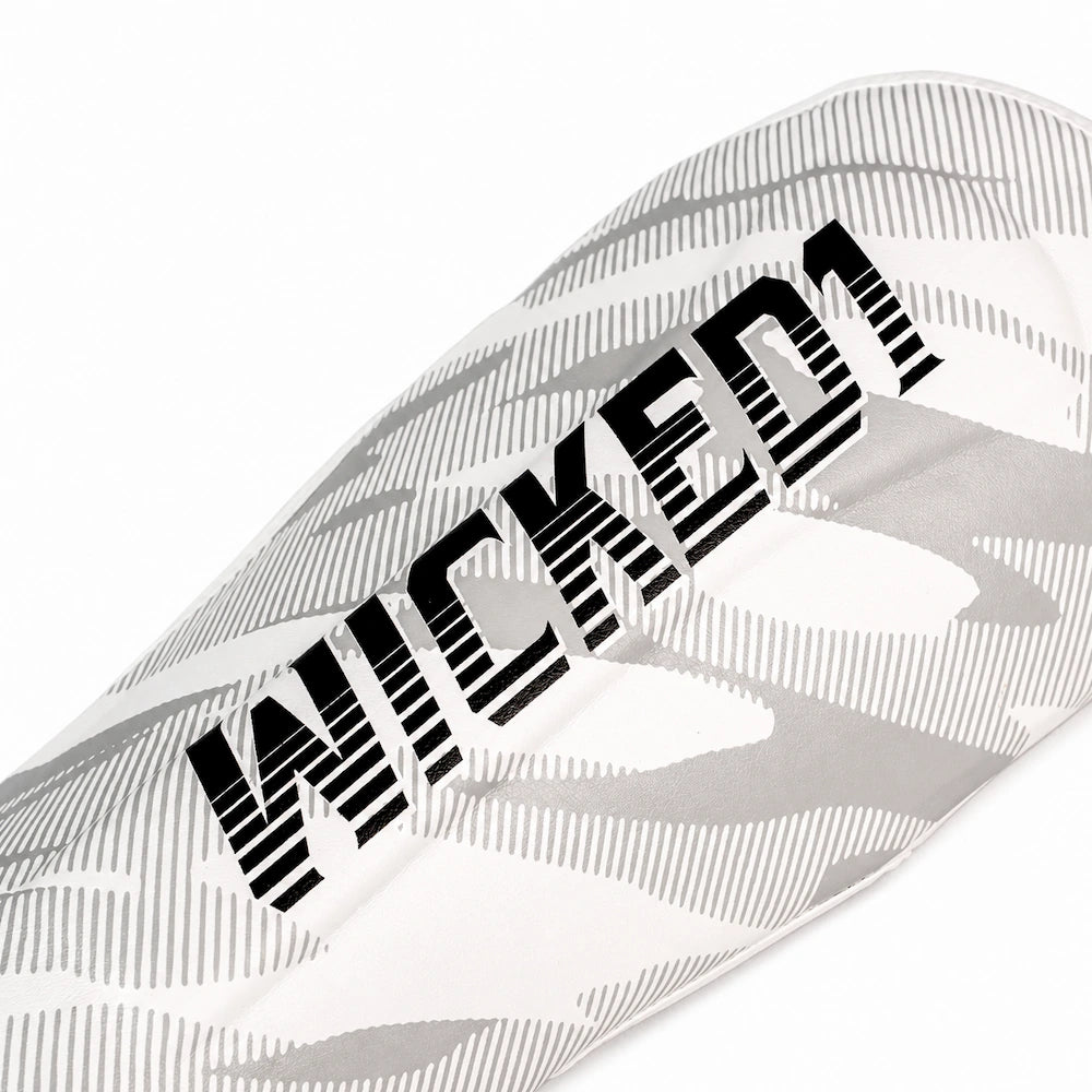A close-up of a white shin guards featuring a gray abstract pattern and the word 'WICKED' printed diagonally in bold black letters.