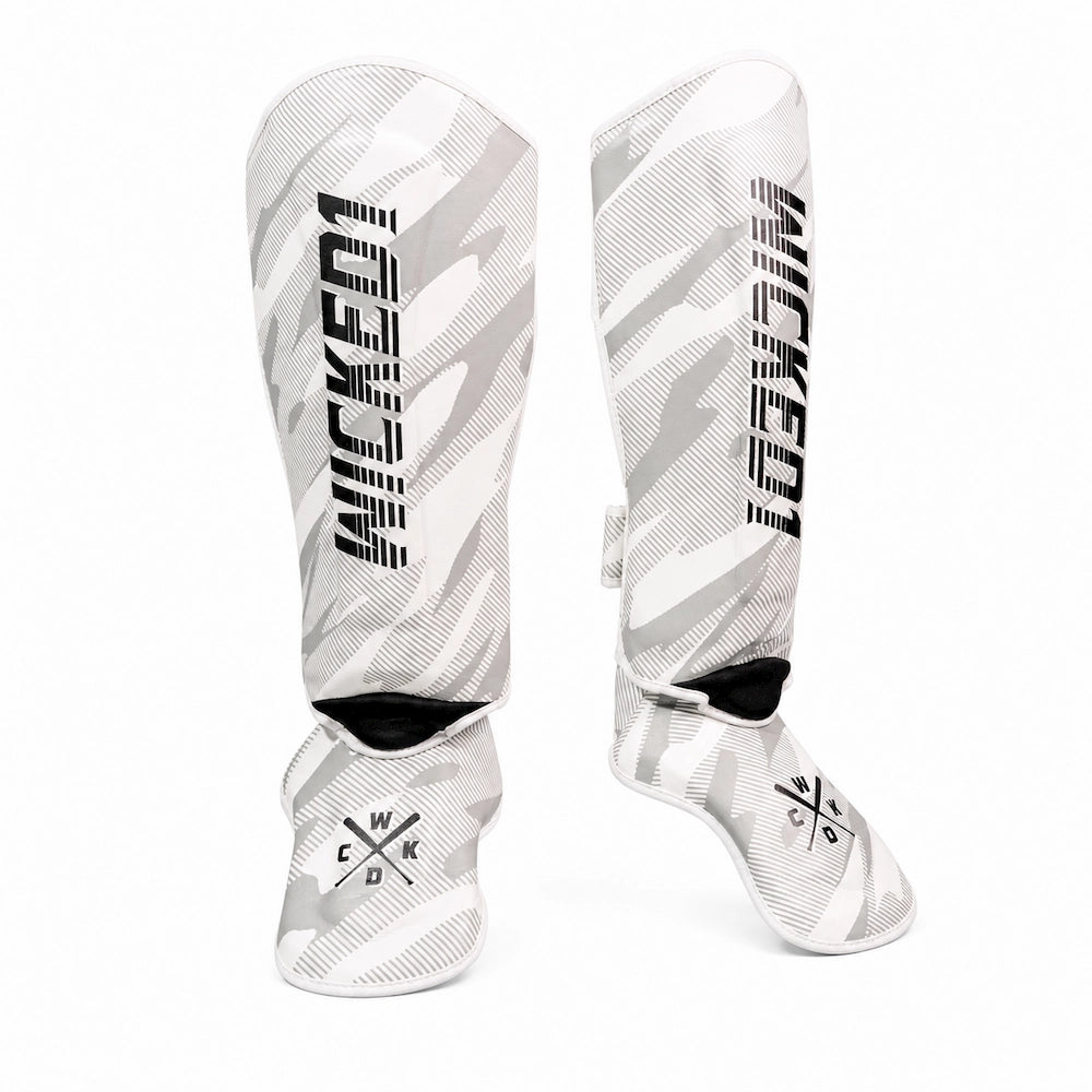 A pair of white and gray camouflage shin guards with black 'WICKED1' branding printed vertically on the front, displayed against a solid white background.