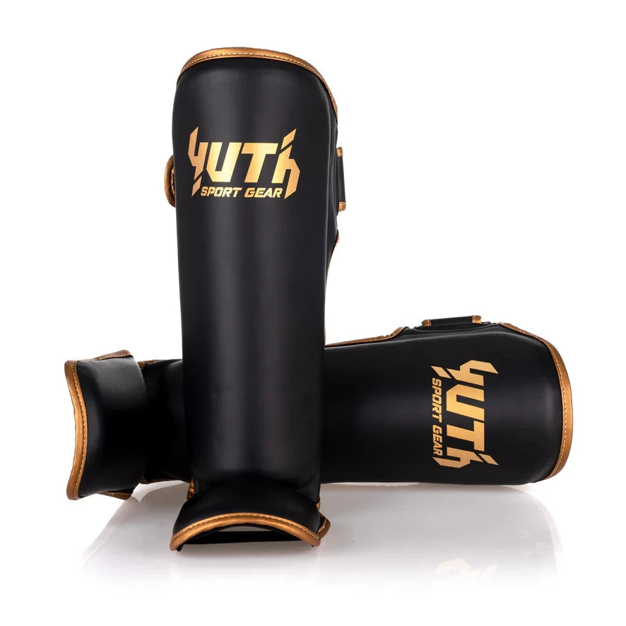 Black shin guards with gold YUTH logo on a white background