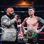 Two boxers standing face-to-face with championship belts around their necks, likely in a boxing ring.