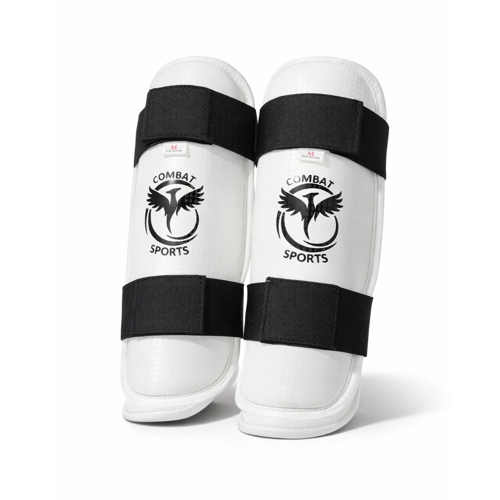 Pair of white taekwondo shin guards with black straps and 'Combat Sports' logo on a white background