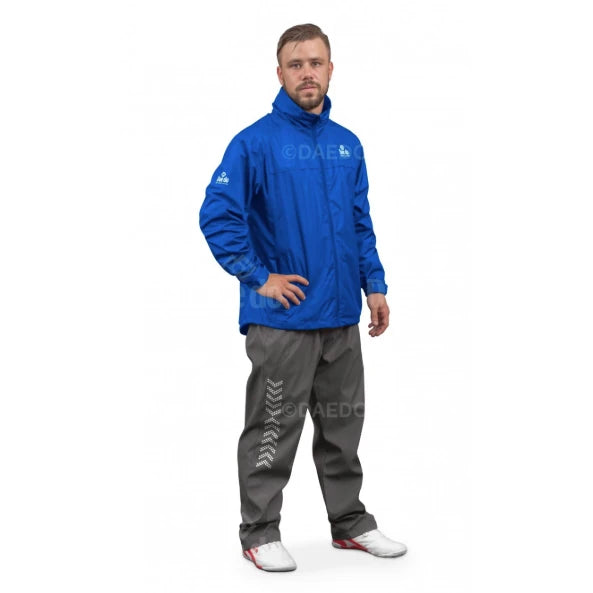 Man wearing a blue windbreakfer and gray pants with visible branding on a white background