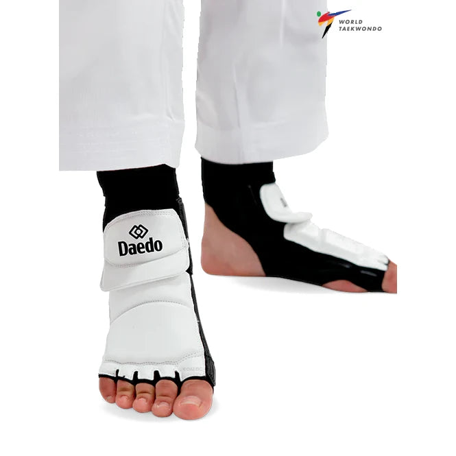 White and black Daedo foot guards on a person's feet with World Taekwondo logo.