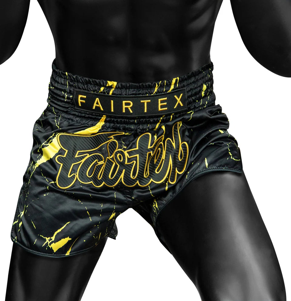 Black and yellow Fairtex boxing shorts on a person against a white background