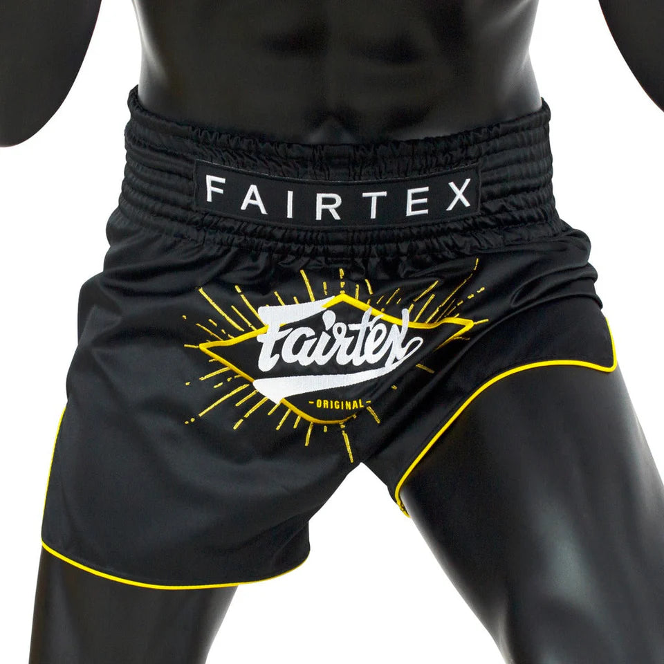 Black Fairtex Muay Thai shorts with yellow accents on a mannequin against a white background