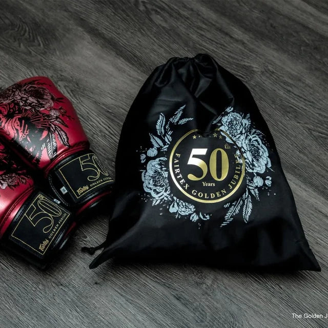 Red boxing glove with '50' logo next to a black drawstring bag with '50' logo on a wooden surface