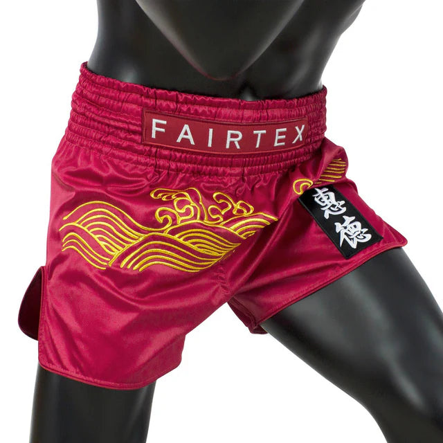 Red Fairtex Muay Thai shorts with yellow designs on a white background