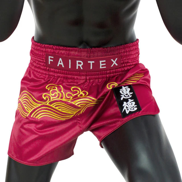 Red Fairtex Muay Thai shorts with gold designs on a white background