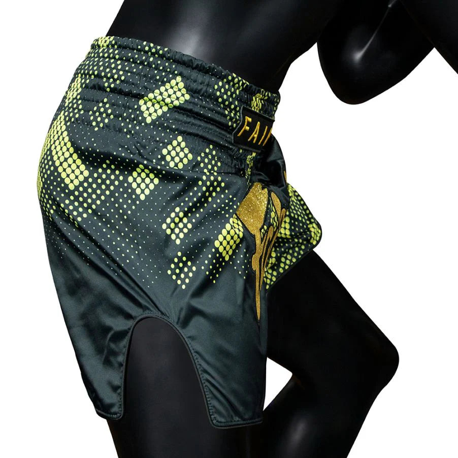 Green and yellow patterned Muay Thai shorts on a mannequin against a white background
