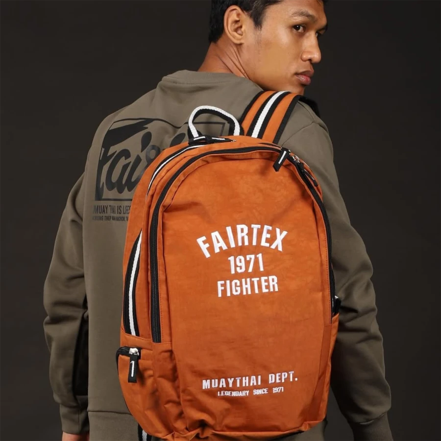 Male wearing an orange Fairtex backpack with a dark background