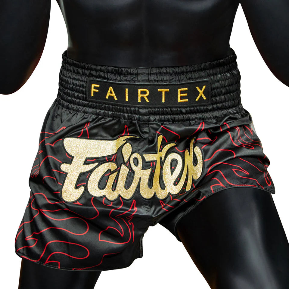 Black Muay Thai shorts with red patterns and Fairtex branding on a white background