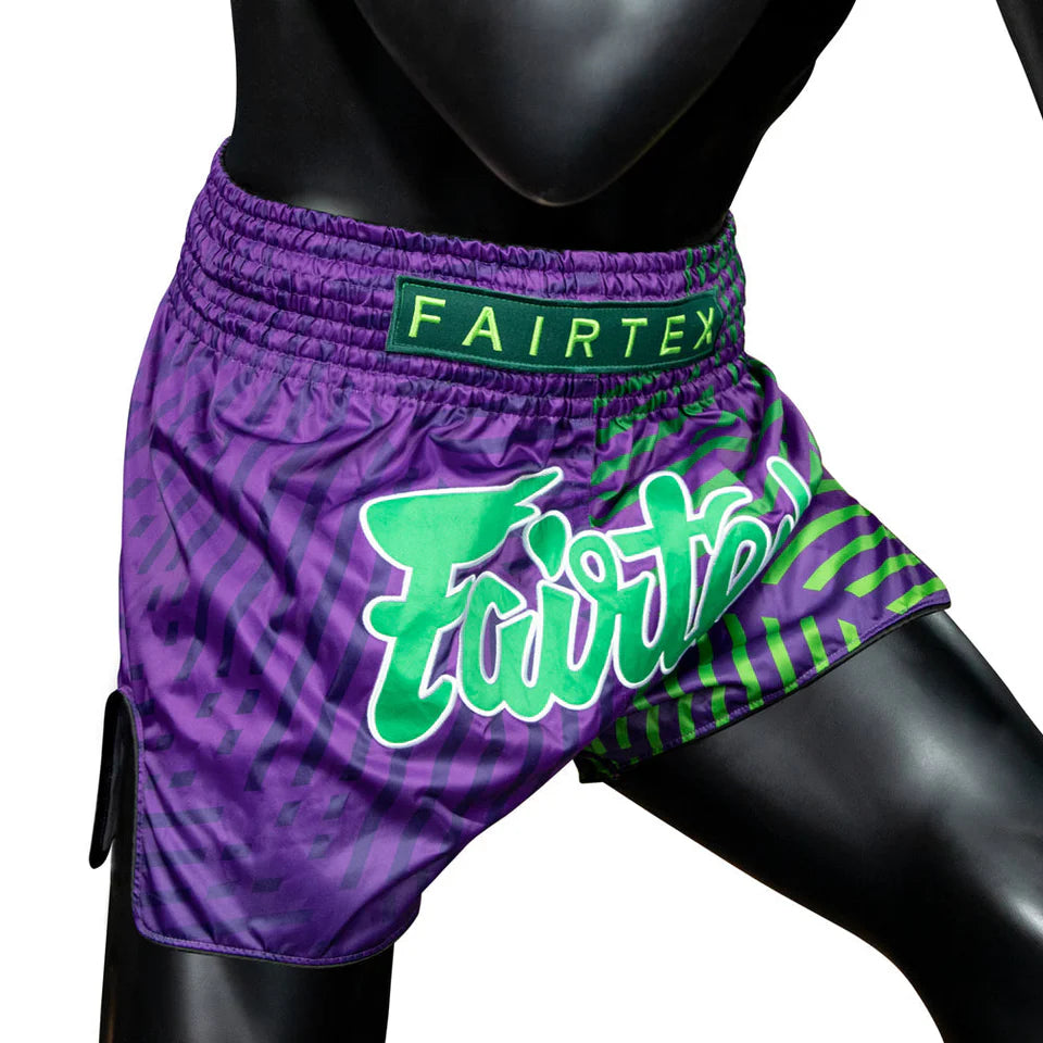 Purple Muay Thai shorts with green patterns and Fairtex branding on a mannequin.