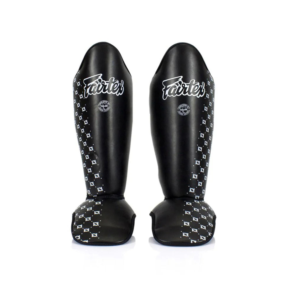 Pair of black shin guards with white patterns and 'Fairtex' branding on a white background