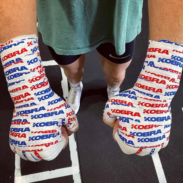 Person wearing boxing gauze and tape with 'Kobra' branding on a dark floor.