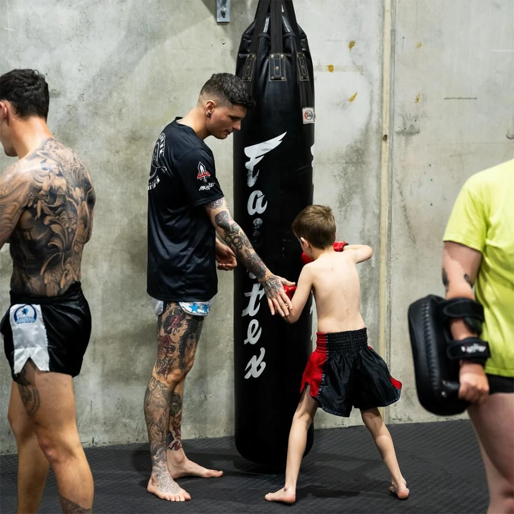 Two adults and a child in a martial arts training session with a punching bag.