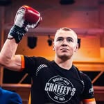 Person wearing boxing gloves and a 'Chaffey's' shirt in a boxing ring.