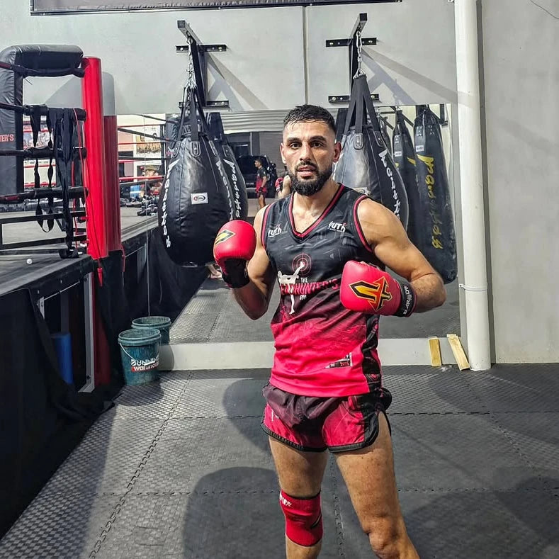 Boxer in red and black gear posing in a gym.