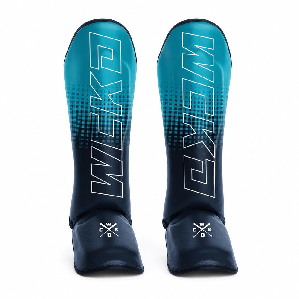 A pair of WICKED 1 Muay Thai shin guards in a teal-to-dark-blue gradient, featuring white vertical branding and a white crossed-kick logo near the bottom, set against a plain white background.