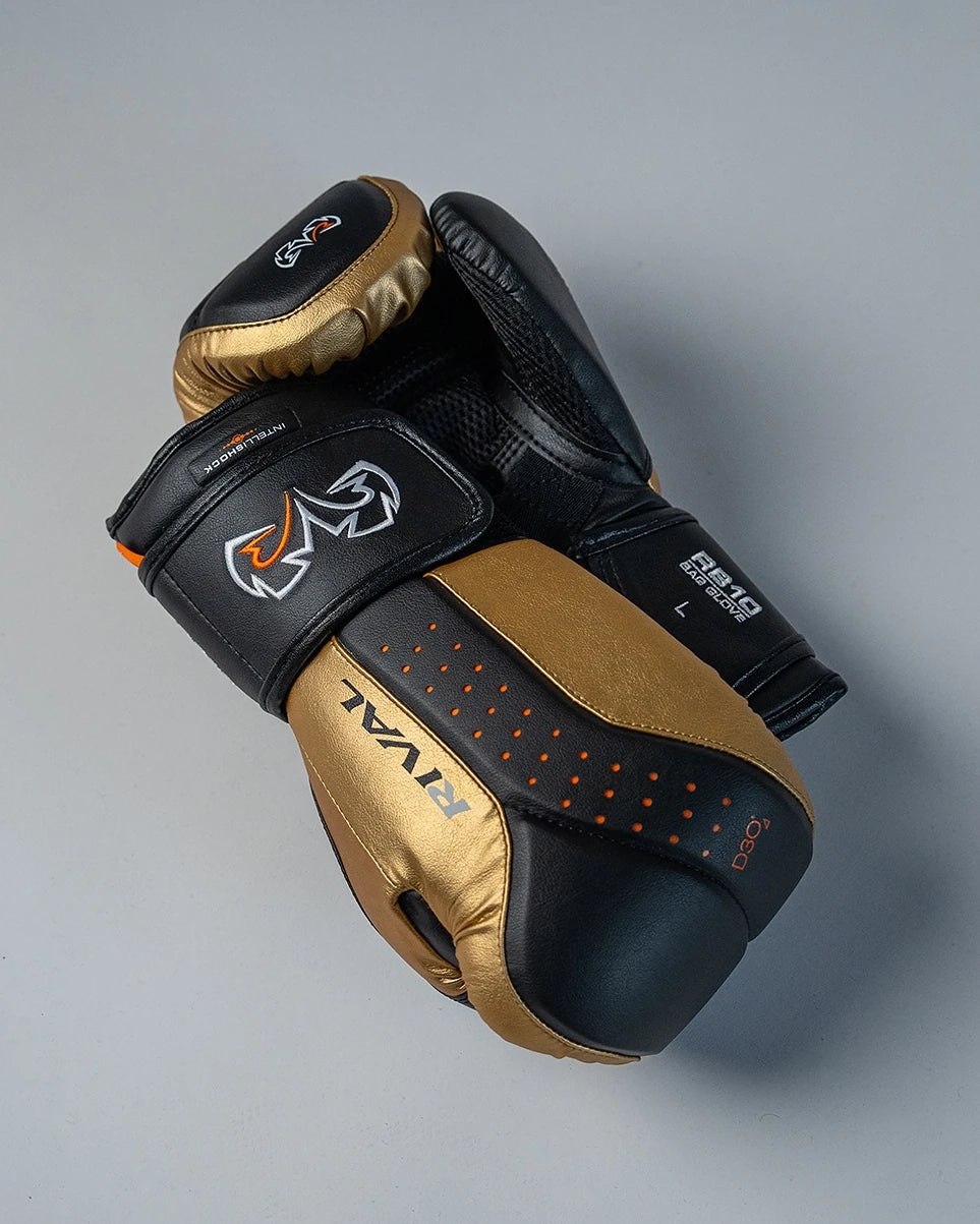 A pair of Rival RB10 boxing gloves in black and gold, displayed on a neutral gray background.