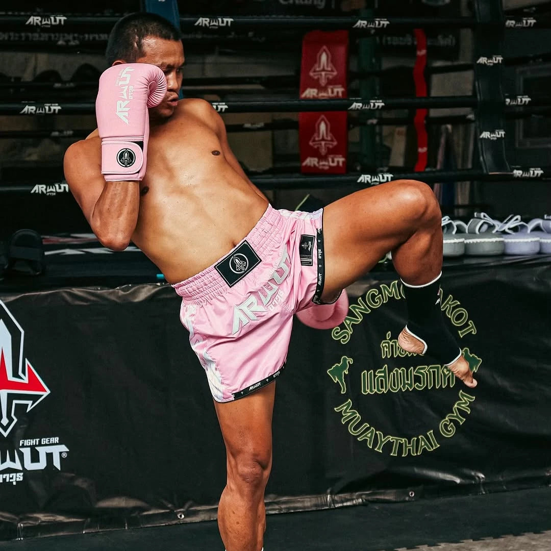 Seksan in pink Arwut boxing shorts and gloves performing a knee infront of a boxing ring.