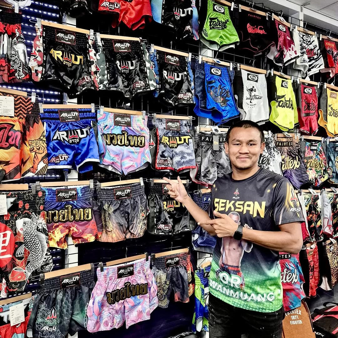 Man standing in front of a display of colorful Muay Thai shorts in a store.