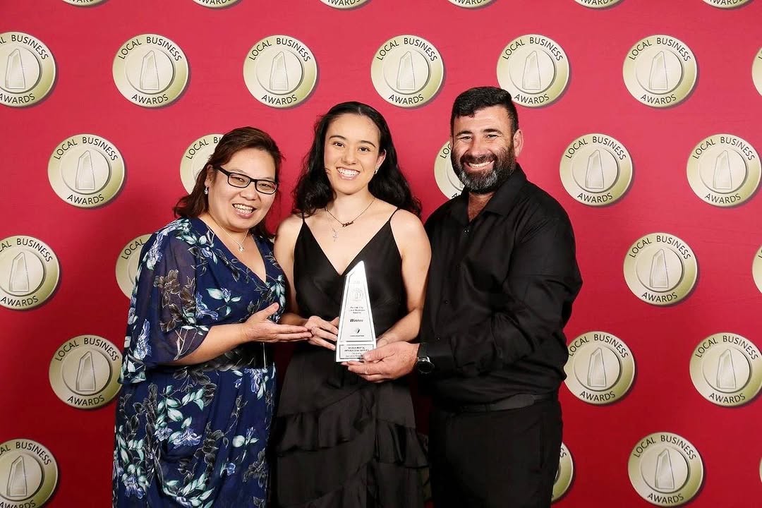 Three people holding an award in front of a red backdrop with logos