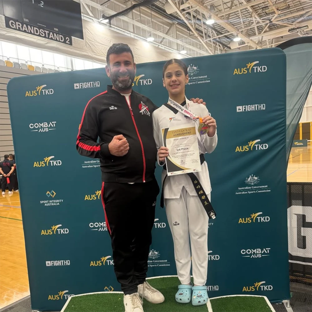 Two individuals standing in front of a branded backdrop with 'AUS TKD' and 'Combat AUS' logos.
