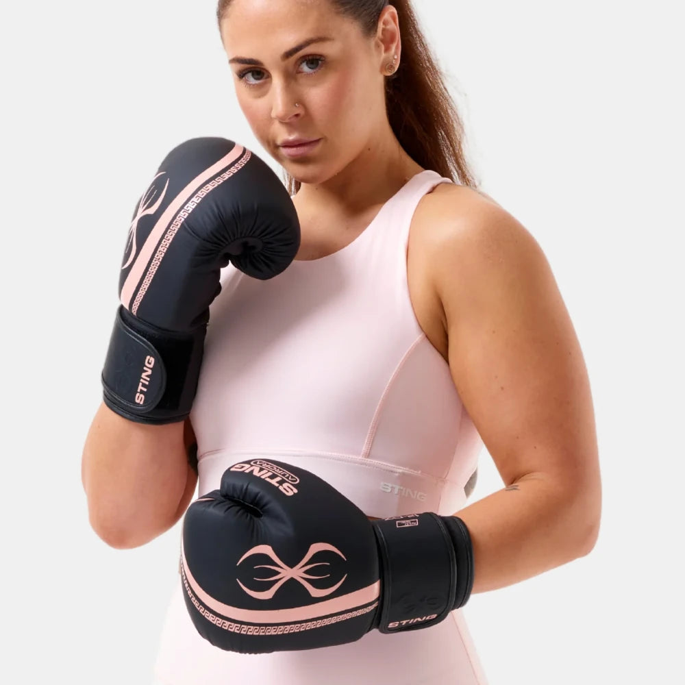 Woman wearing black Sting Sports Aurora boxing gloves with pink accents on a white background