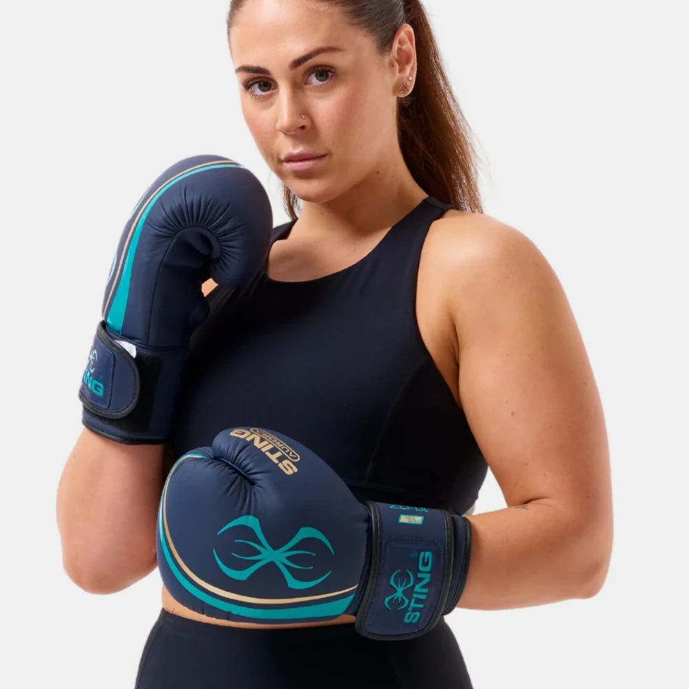 Woman wearing black athletic wear and blue Sting Sports Aurora boxing gloves with a visible brand logo on a light gray background