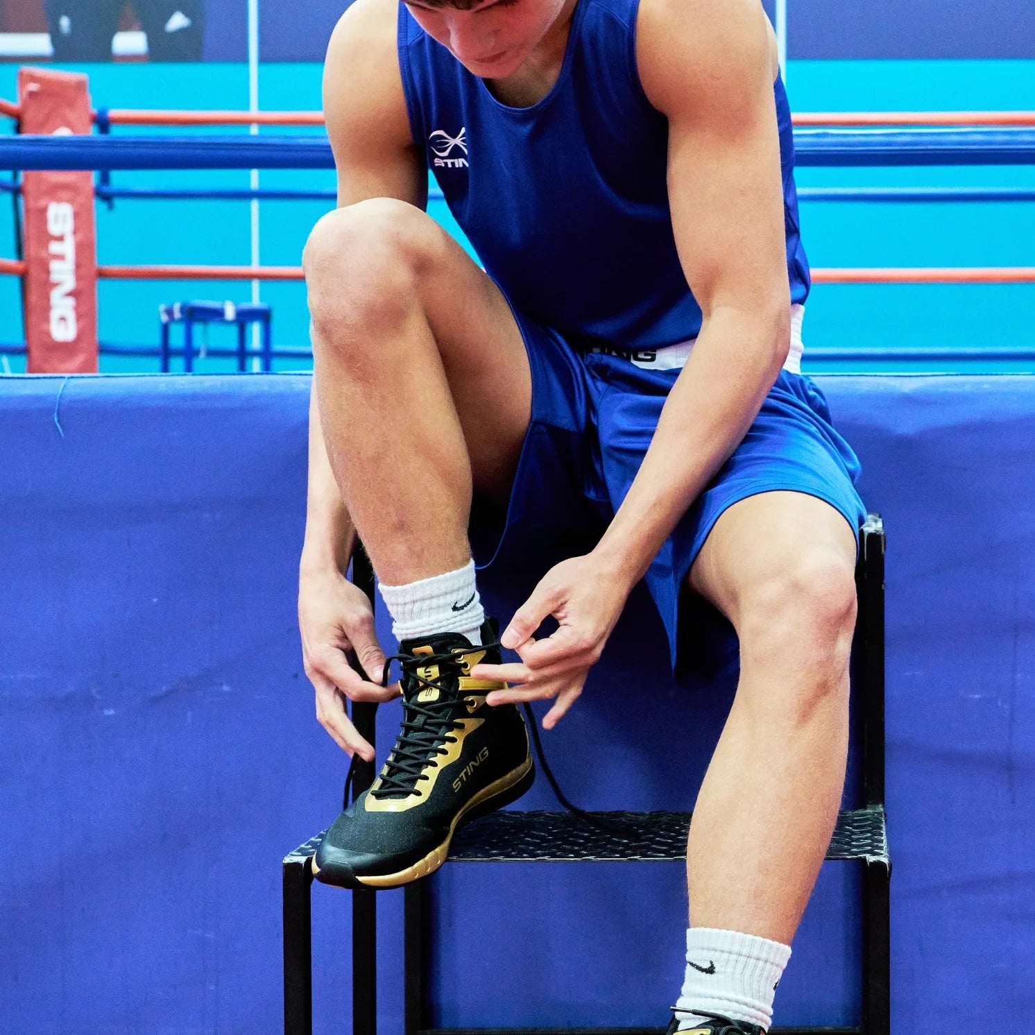 Boxer in blue AIBA apparel tying shoelaces on a blue boxing ring