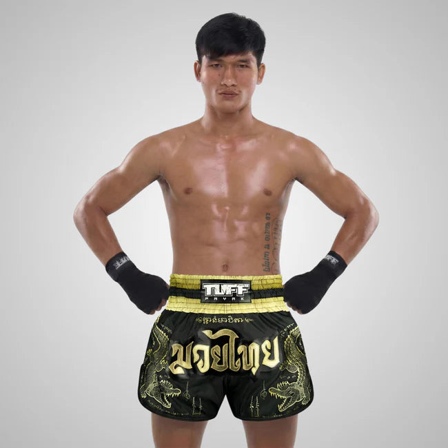 Man wearing black and gold boxing shorts with 'TUFF' branding on a gray background