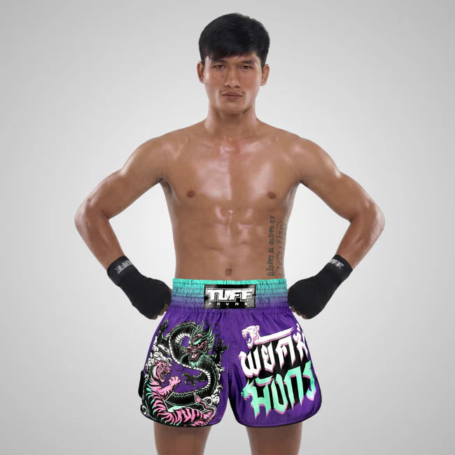 Man wearing colorful Muay Thai boxing shorts with a brand logo on a gray background