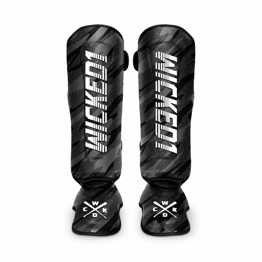 A pair of black and gray camouflage Muay Thai shin guards with bold white 'WICKED1' branding on the front, displayed against a solid white background.