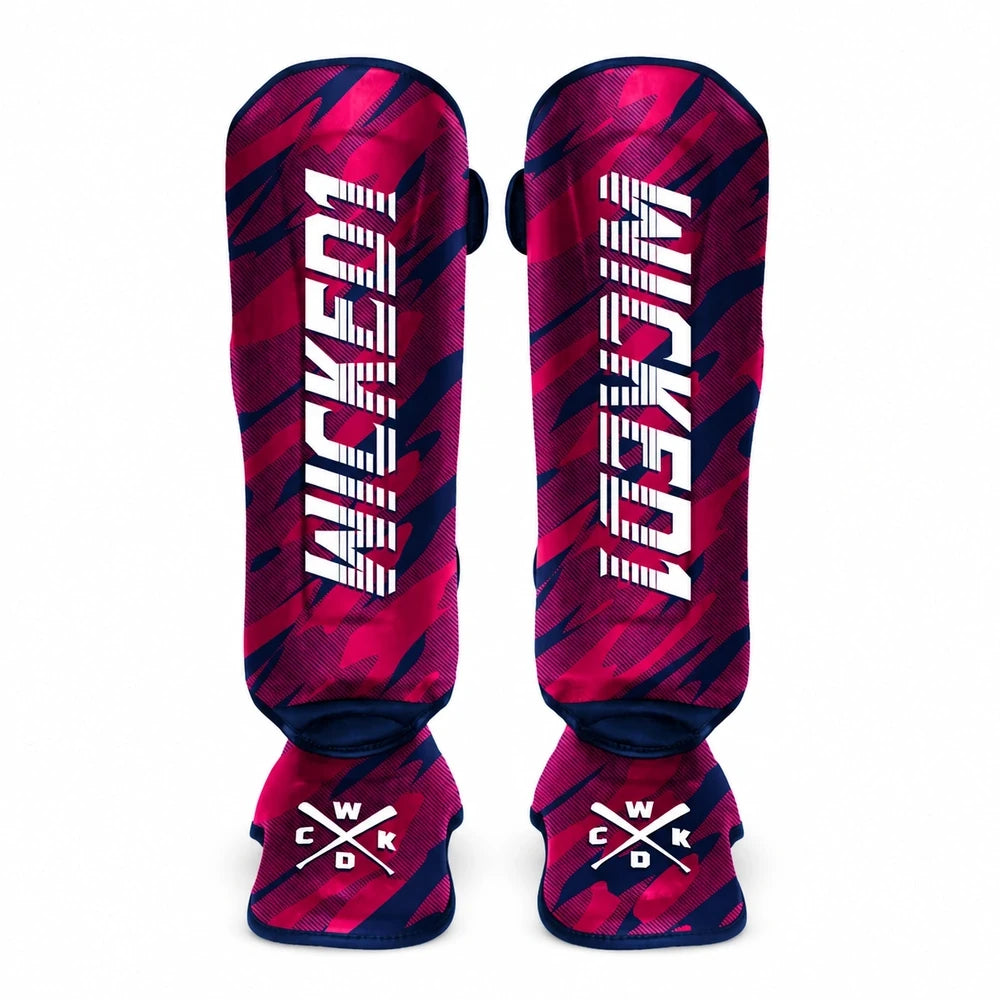 A pair of shin guards featuring a vibrant pink and dark navy blue abstract pattern, with the brand name 'WICKED1' printed vertically in white on each piece. The bottom of each guard displays a white logo with crossed hockey sticks and the letters 'WCKD'.