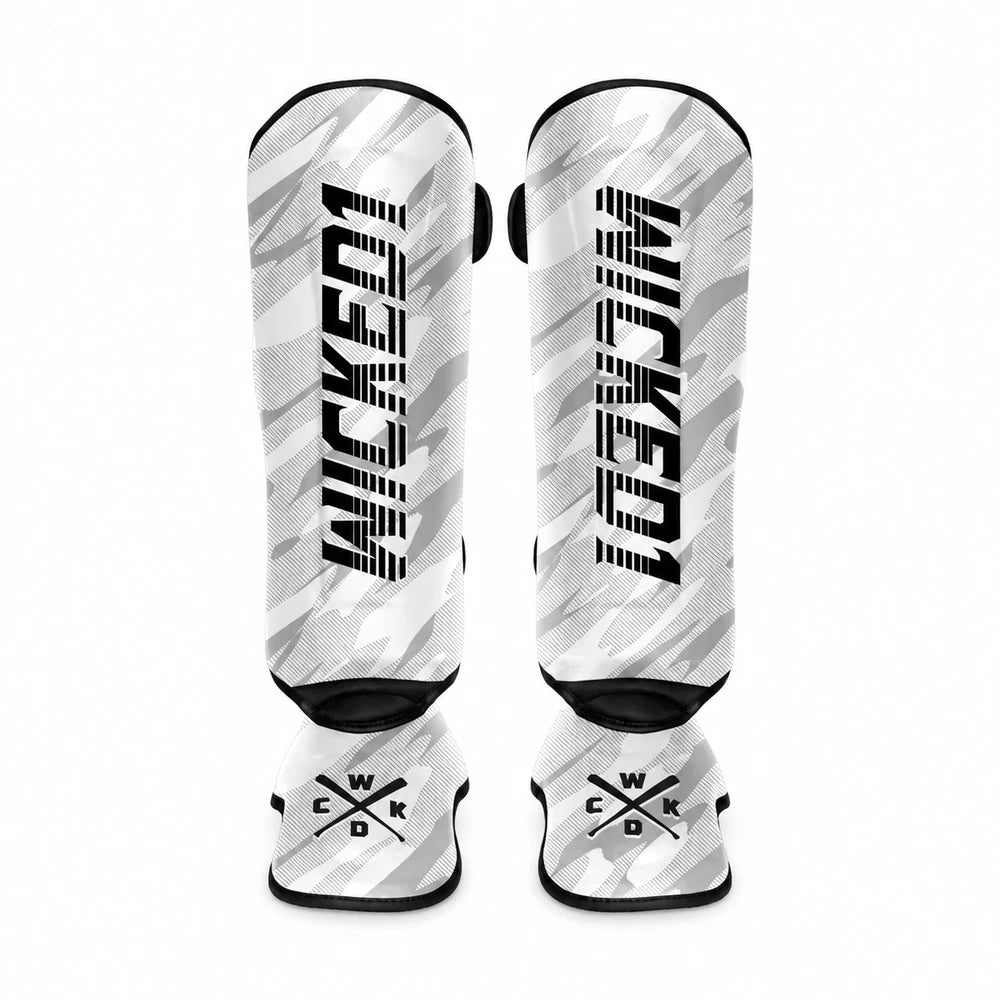 A pair of shin guards featuring a white and gray camouflage pattern with bold black 'WICKED1' branding on the front and crossed 'WKD' logos on the lower section, set against a plain white background.
