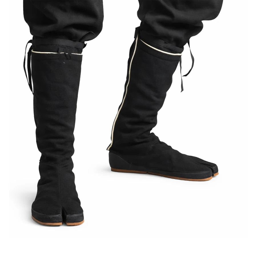 Black tabi boots with white trim worn by a person on a white background