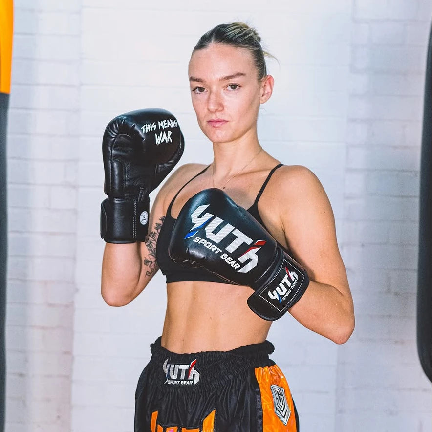 Woman wearing YUTH boxing gloves and muay thai shorts in a training setting